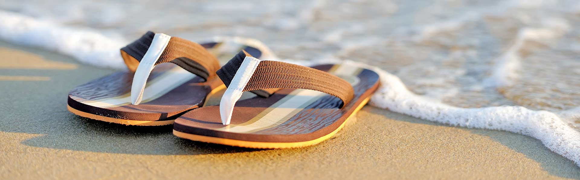 brown sandals on beach with wave water foam