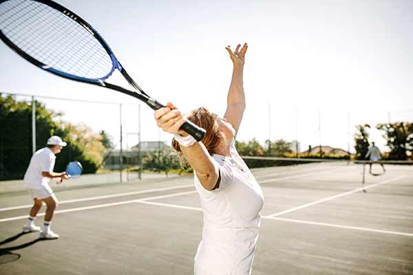 senior woman serving a tennis ball on a court